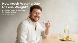 A smiling woman holds a glass of water next to a water bottle and lemon slices, illustrating how much water a day to lose weight effectively.